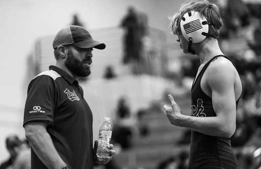 A greyscale image of a Coach talking to boy wearing a high quality custom coaches polo shirt while coaching wrestler wearing custom wrestling uniform.