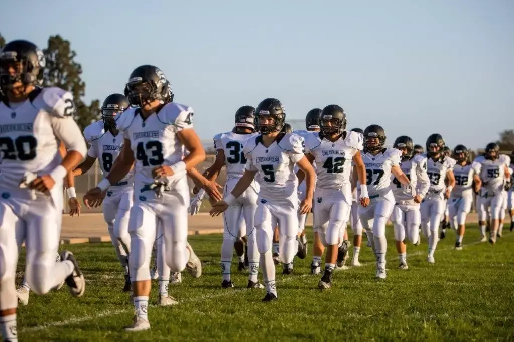 Football team running together wearing white football uniforms by Wooter.