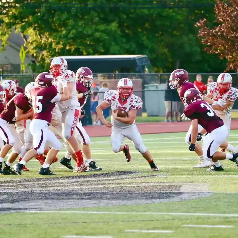 Football player running with ball wearing custom football uniform around offensive players. Custom football uniform designed and manufactured by Wooter.
