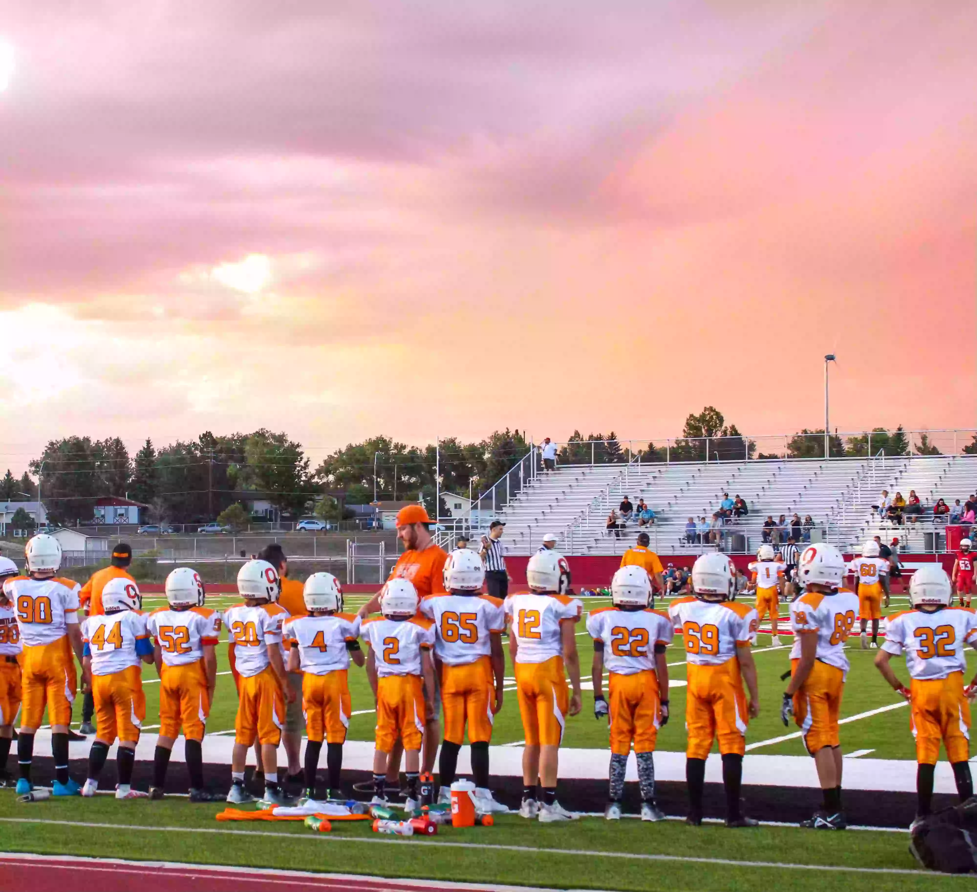 Football team in line up wearing orange and white custom football uniforms.